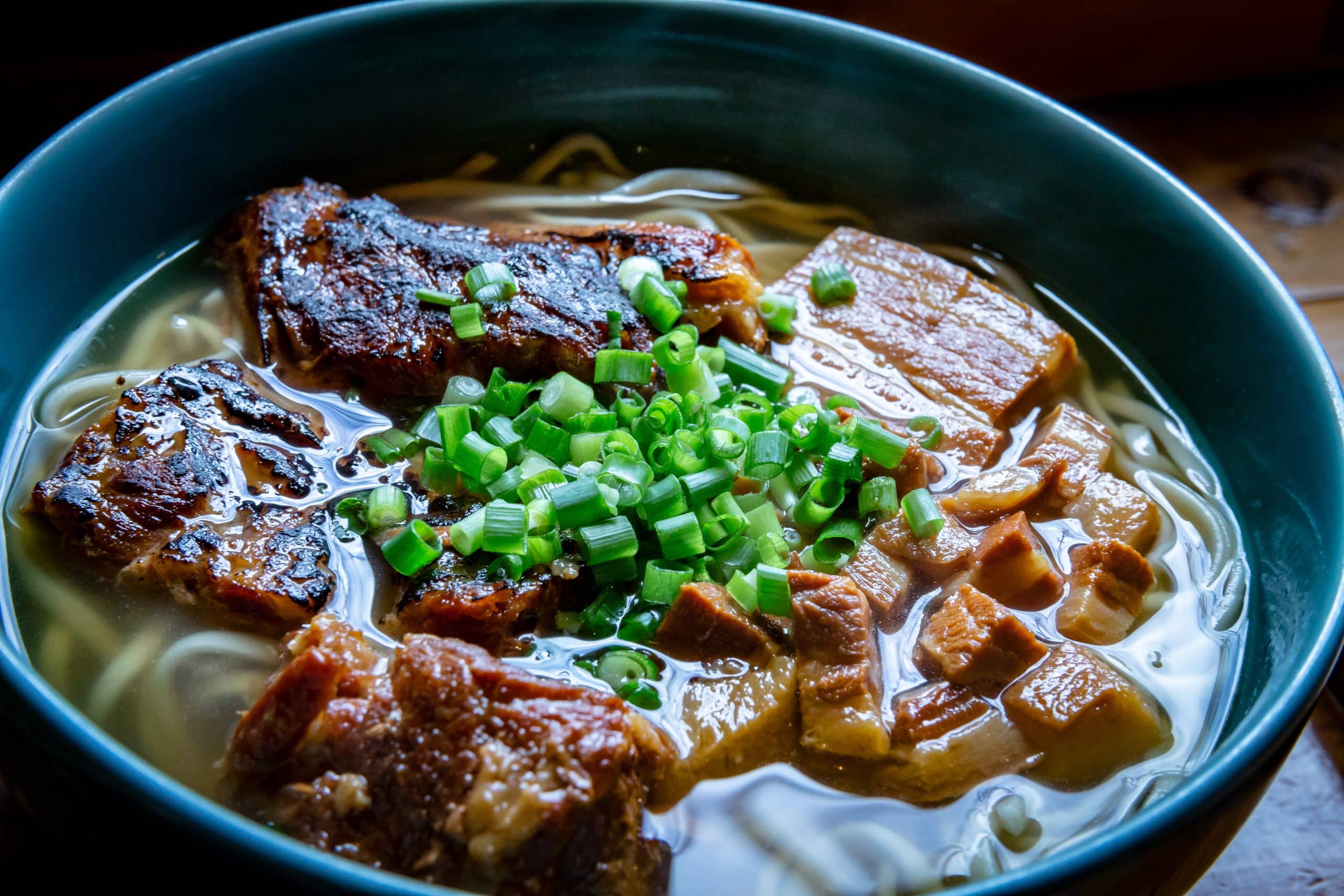 Very attractive bowl of Japanese food showing noodles, pork, broth and topped with green onions